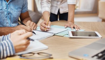 Close up detail of team working o new project in coworking space, writing ideas, looking through graphics on tablet and laptop. Teamwork, business concept.