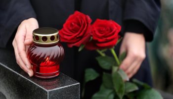 Téléchargez-les-photos-:-Femme-tenant-des-roses-rouges-près-de-pierre-tombale-en-granit-noir-avec-bougie---en-image-libre-de-droit